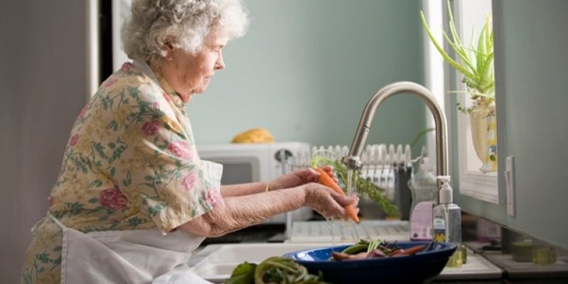 senior woman washing vegetables in kitchen sink